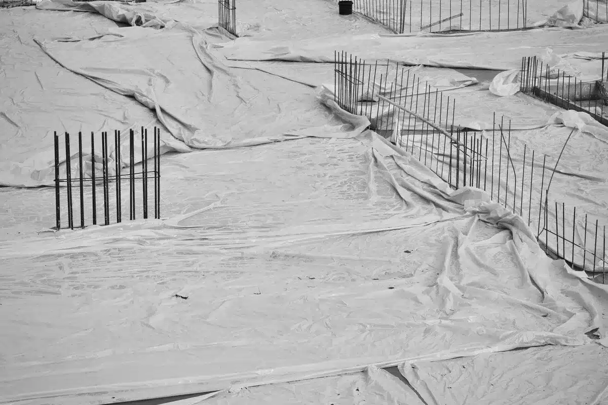 An empty construction site on the White House grounds, exposed concrete and steel framework rising against the sky, the East Wing location marked by raw materials and machinery, security barriers surrounding the perimeter, captured from a distance