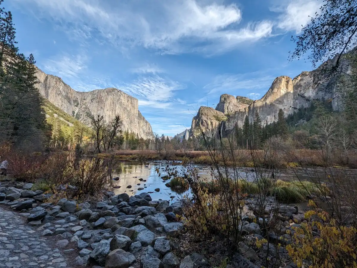 A pristine mountain valley with granite cliffs and ancient sequoia groves rising above a quiet meadow, untouched wilderness stretching to distant peaks