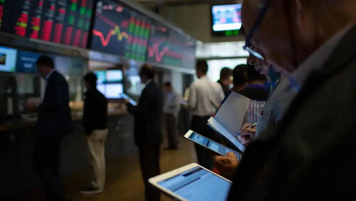 Stock market trading floor with multiple screens showing red and green price movements, traders focused on data | stock market volatility tech stocks