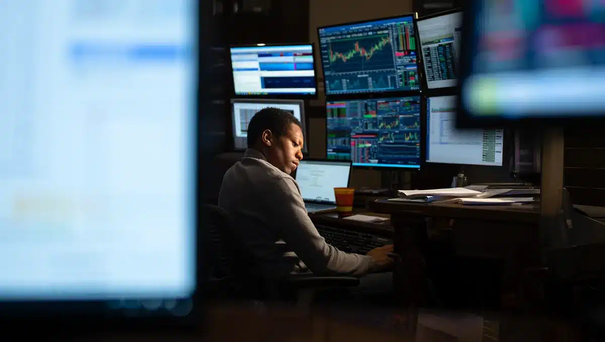 Financial analyst monitoring stock market data on multiple screens showing real-time ticker symbols and candlestick charts, bright colors reflecting off glass surfaces, tension in focus | stock market trading screens earnings