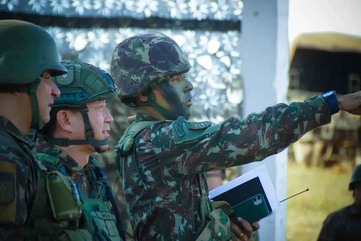 Military operations center with multiple screens displaying real-time drone feeds and AI-detected target annotations, tactical data visualizations, and command staff monitoring automated threat identification systems in a secure facility.