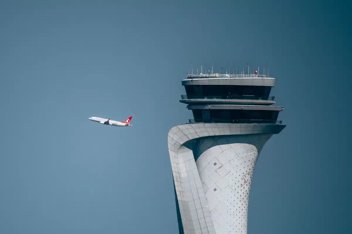 A busy airport control tower overlooking multiple taxiways with aircraft lined up, runway markings visible in strong afternoon light, clouds gathering overhead