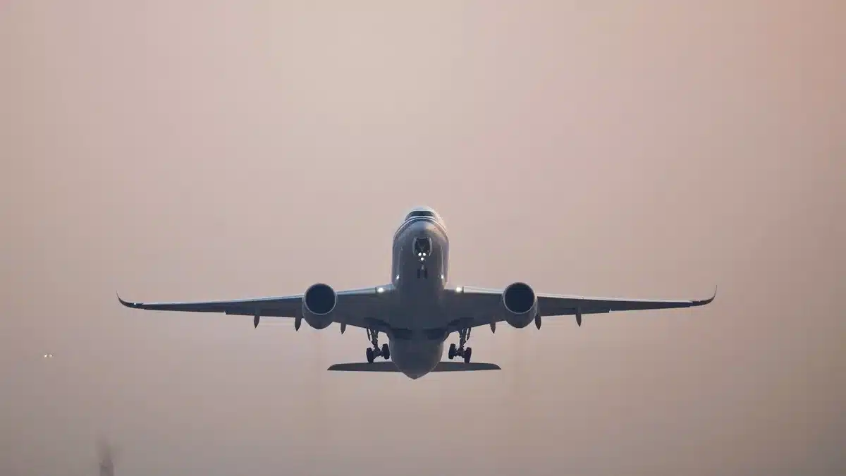 A pristine aircraft silhouette against a dawn sky, wings level, climbing toward a distant coastline, golden light breaking across the horizon.