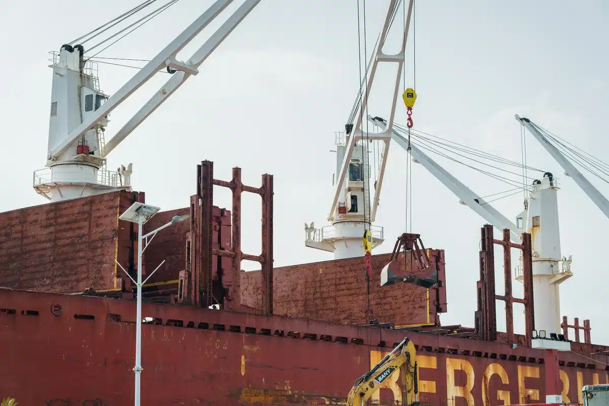A cargo vessel docked at a steel manufacturing facility in Ontario, with industrial equipment visible, representing the impact on Canadian industrial exports.