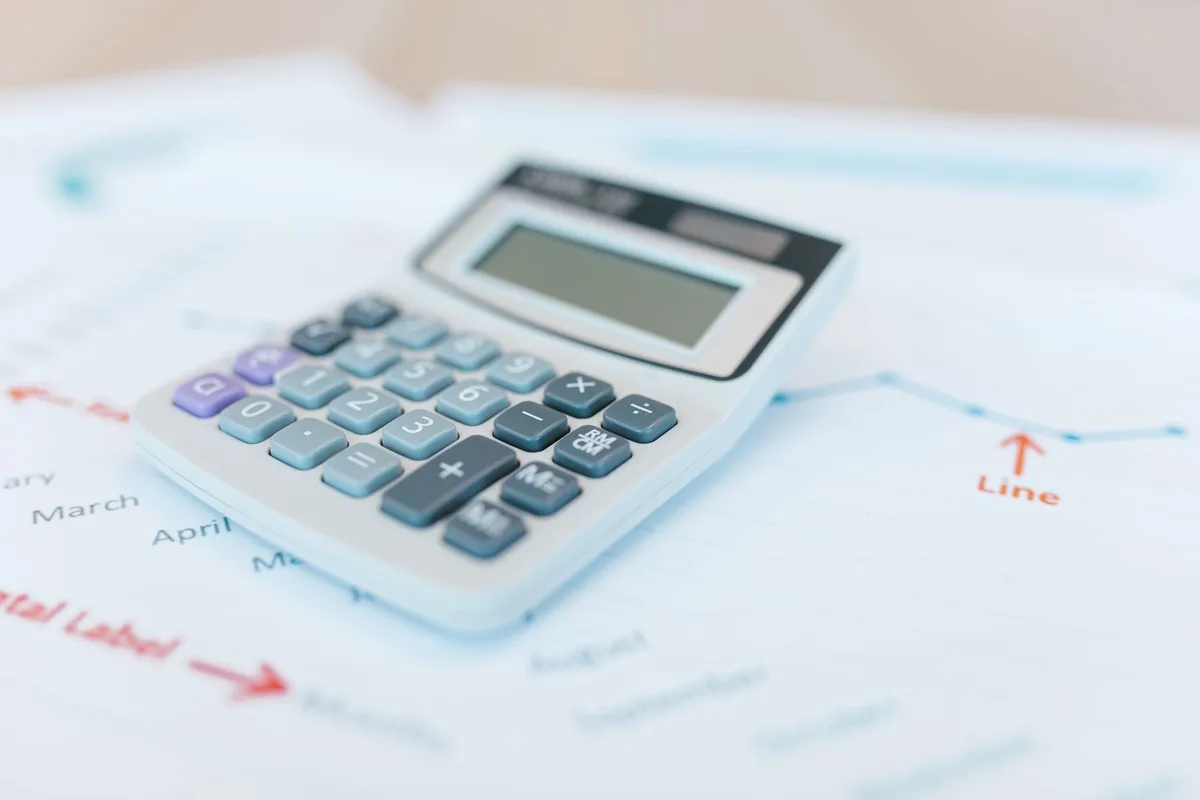 A stack of financial documents and quarterly reports on a desk with a calculator and pen, papers partially illuminated, neutral office background