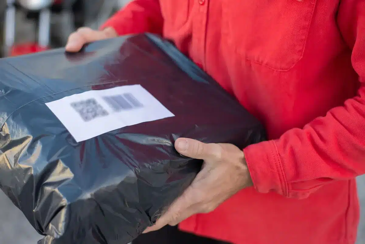 A postal service worker handling ballots at a sorting facility, with ballot envelopes featuring barcodes visible, fluorescent overhead lighting illuminating the workspace