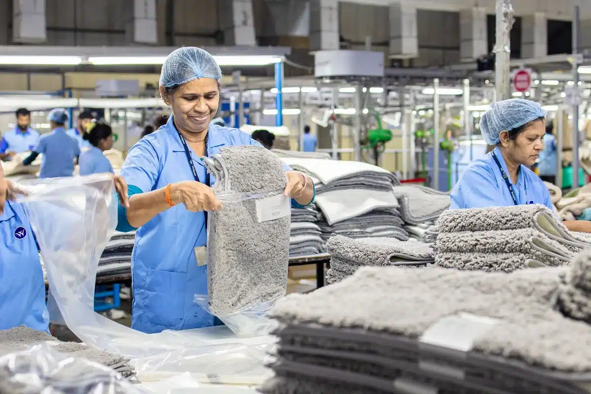 A postal worker sorting mail at a distribution facility counter, focused concentration visible, fluorescent overhead lighting illuminating bundles of envelopes and packages in organized bins.