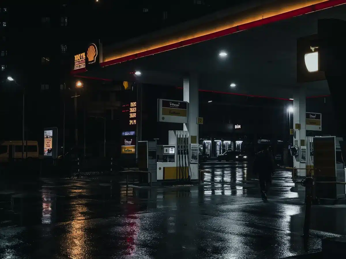 A gas station pump display showing prices above $4 per gallon, with blurred cars and station signage in the background, reflecting the economic impact of the Iran conflict on American consumers