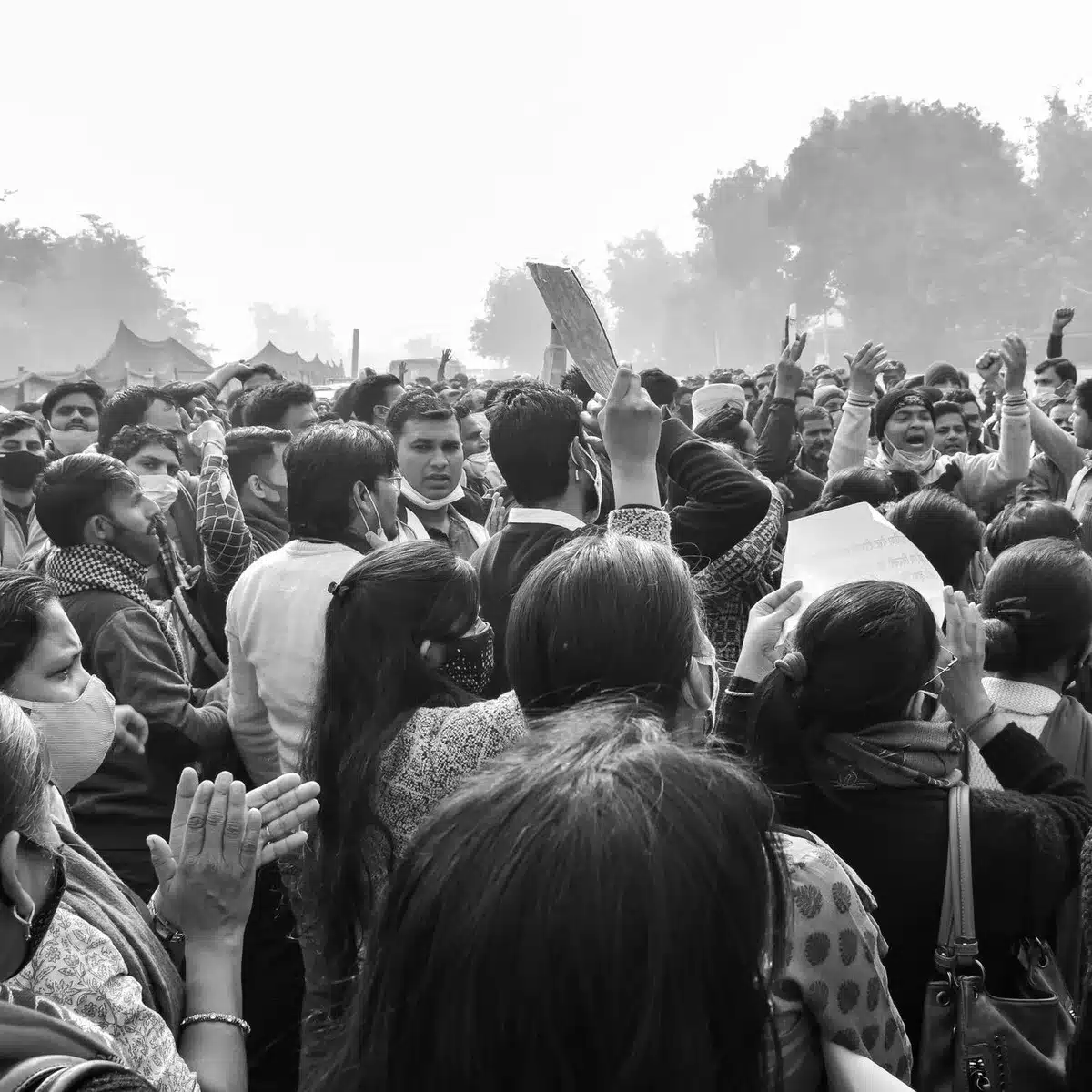 Outdoor campaign rally scene with anonymous supporters holding signs, a podium under bright daylight, diverse crowd silhouettes, jubilant energy