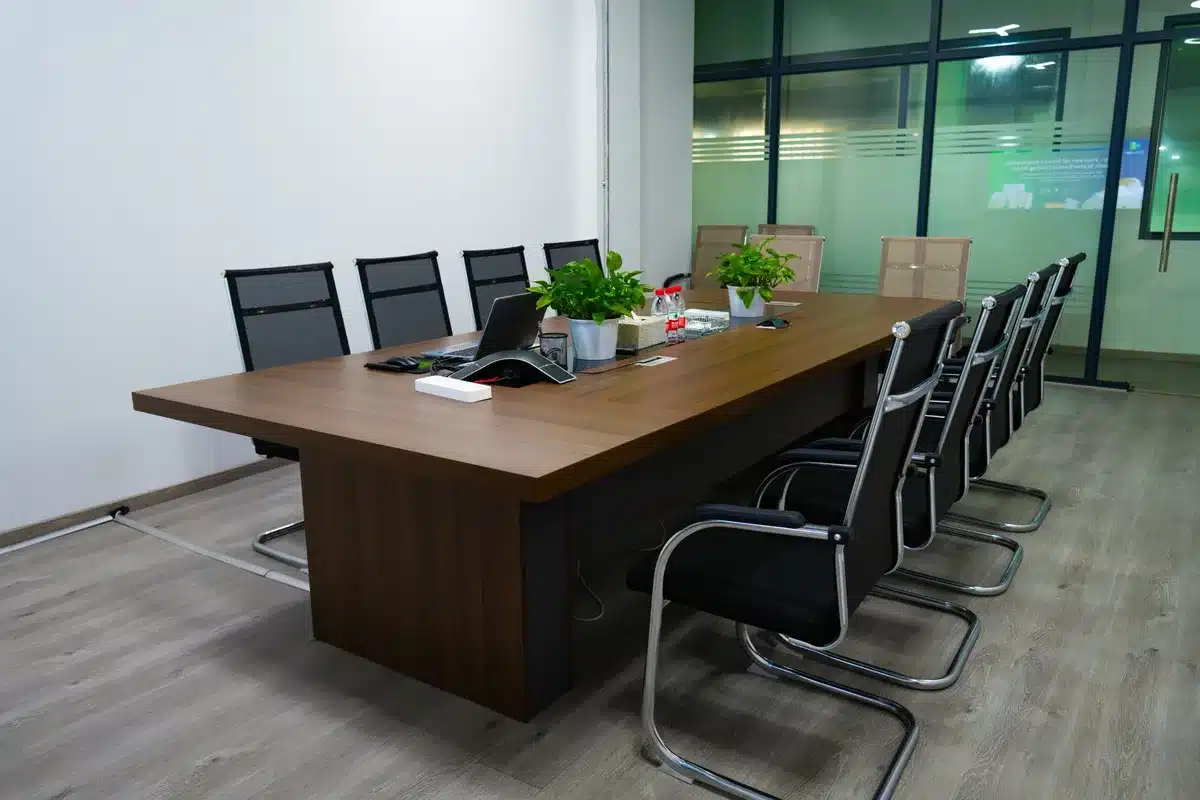 Corporate conference room with empty chairs around a polished table, soft overhead lighting reflecting off glass surfaces, a single pen and notepad visible, suggesting a boardroom where major business decisions are made