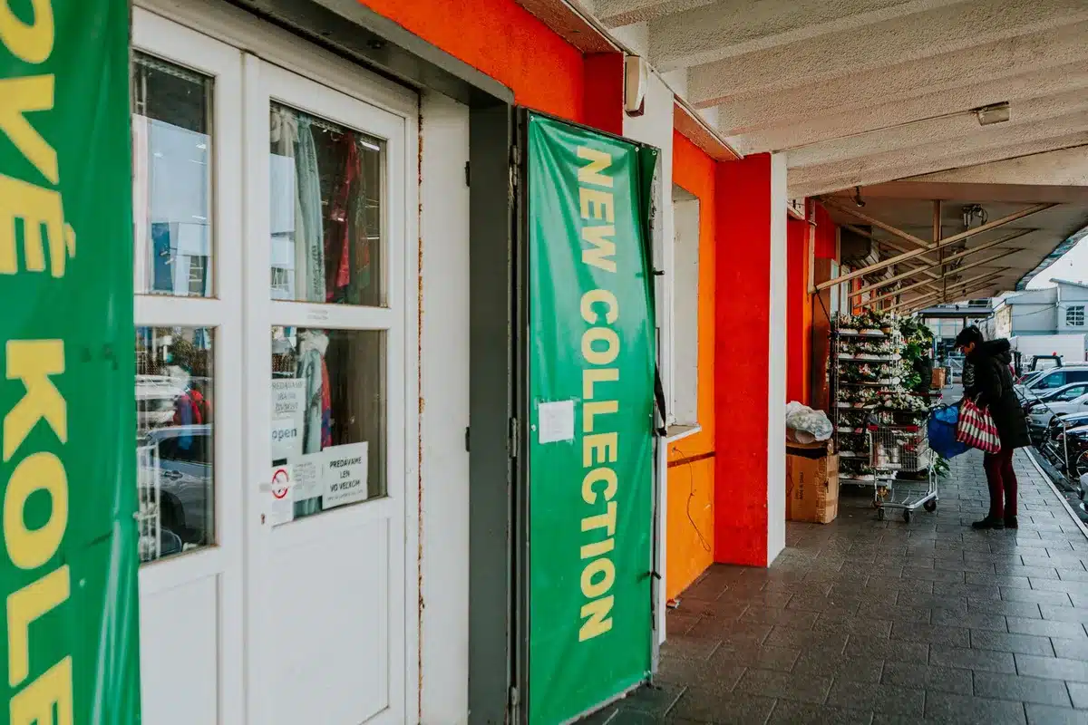 Retail storefront entrance with glass doors and signage, early morning light streaming across the facade, a shopping cart in the foreground, anticipation before opening