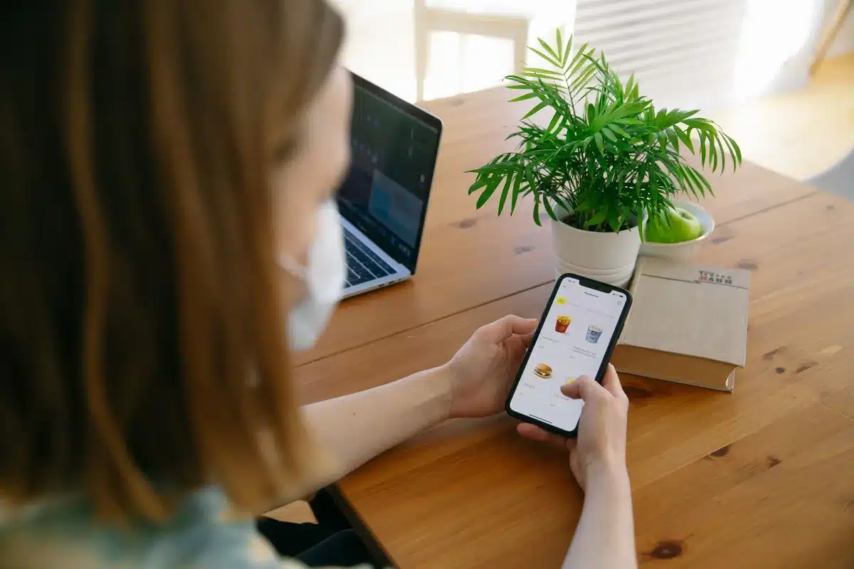 Glowing smartphone screen showing an e-commerce shopping interface, a customer's hand scrolling through products, warm indoor lighting, digital marketplace activity