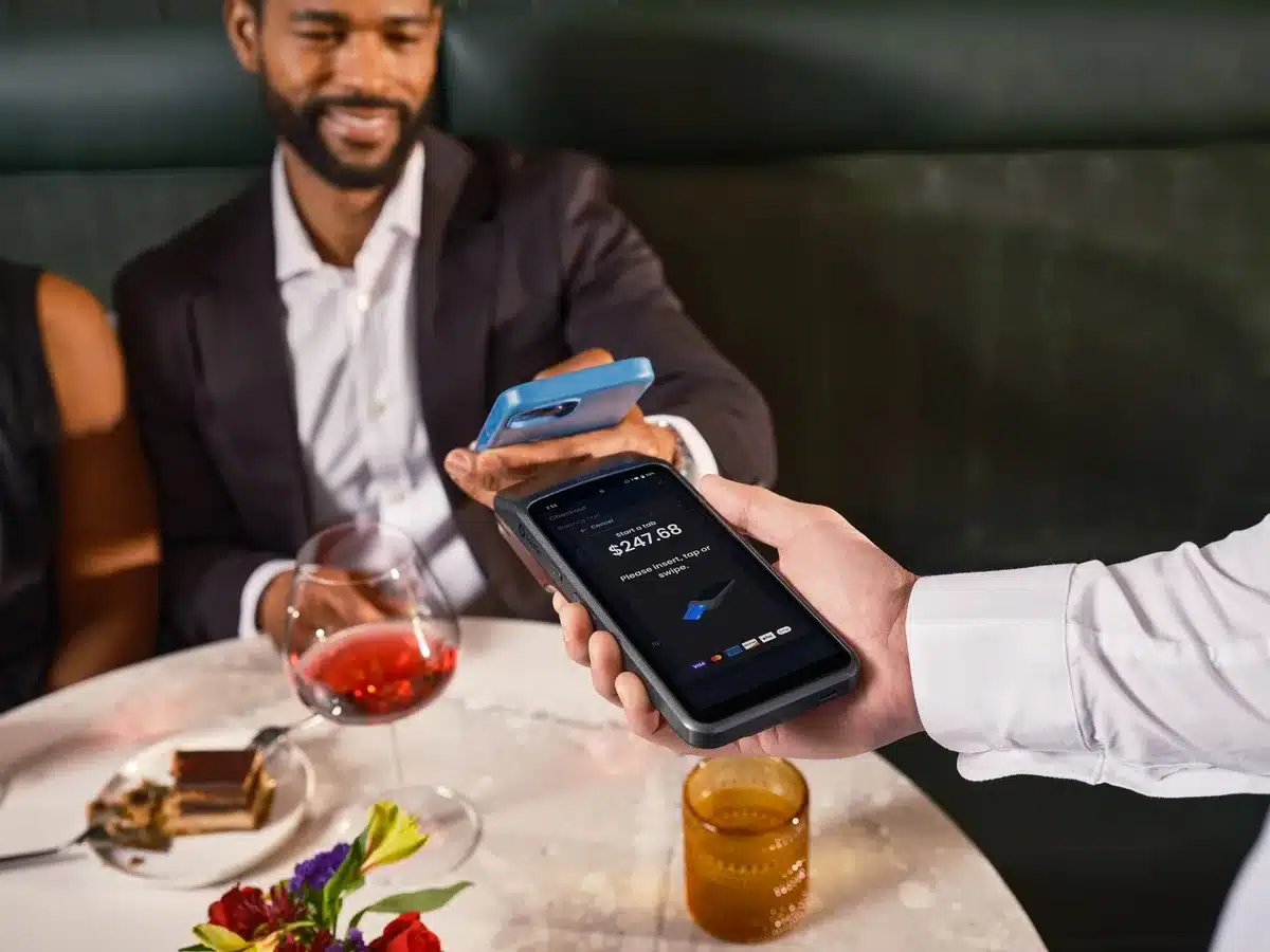 An anonymous customer's hand holding a smartphone near a contactless payment terminal at a retail checkout counter, the screen glowing with payment confirmation, modern minimalist checkout environment