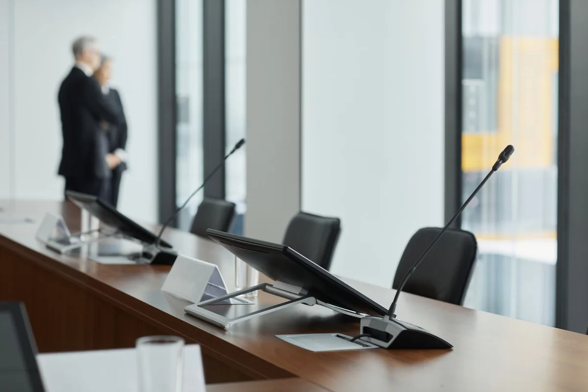 Federal Reserve building interior with a large conference table and empty chairs, cool blue lighting reflecting off polished surfaces, a single gavel on the table