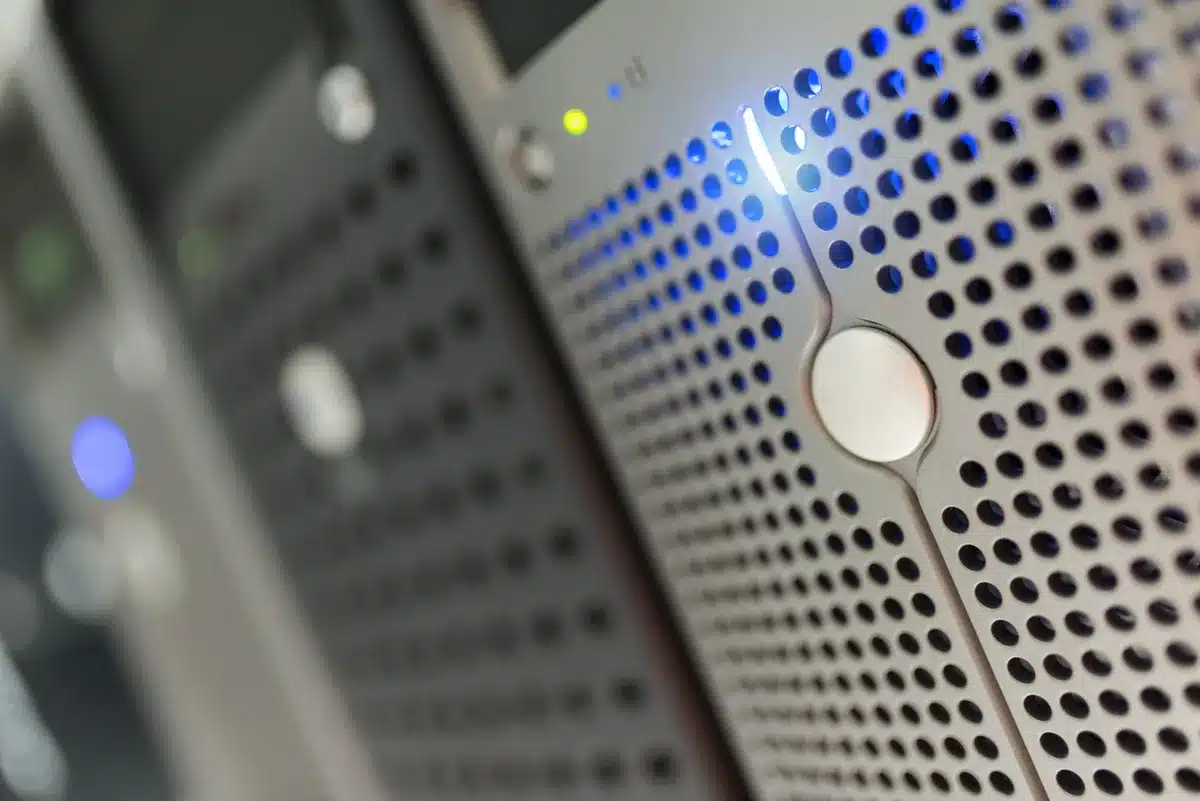 A data center server rack with rows of blinking indicator lights and cooling fans, bathed in cool blue ambient light, suggesting massive computational density and storage demand.
