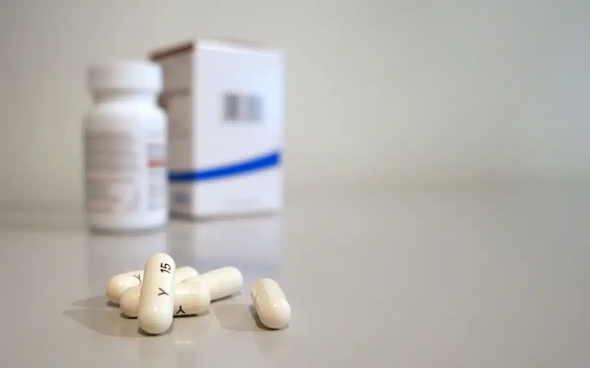 Prescription medication bottles arranged on a pharmacy shelf, white labels catching fluorescent light, blurred shelves of pharmaceuticals receding into background
