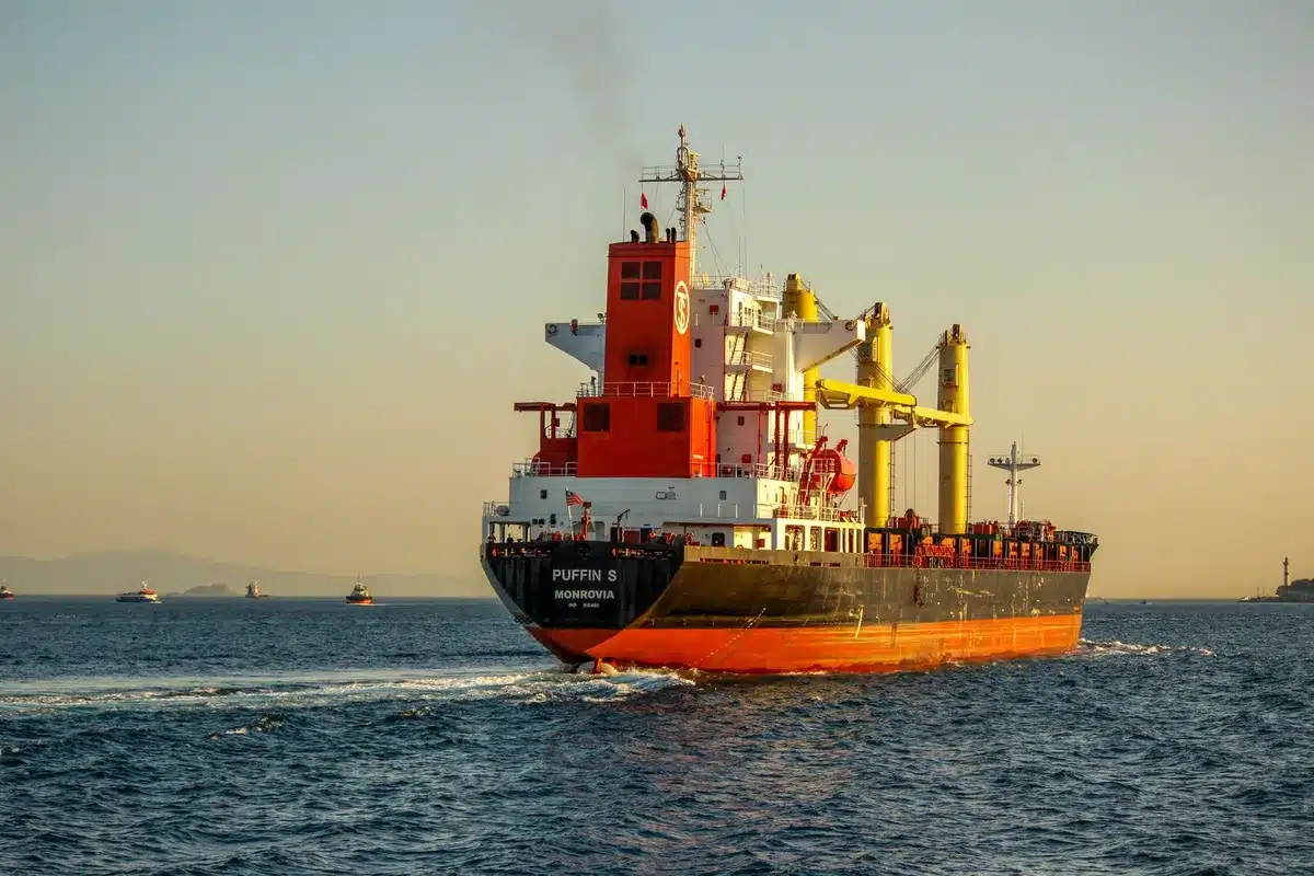 A contested maritime strait with shipping vessels, commercial tankers navigating narrow waters amid geopolitical tension, industrial port facilities visible on distant shores, tension