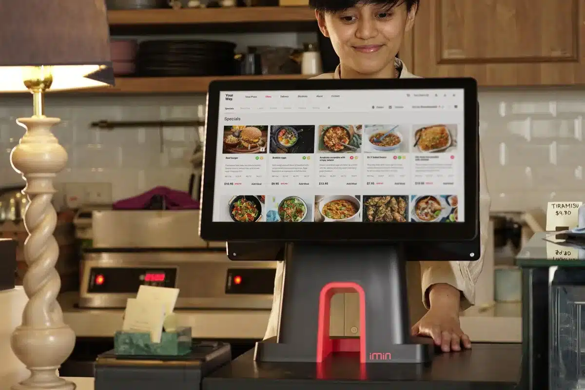 A restaurant employee in a distinctive uniform standing at a counter, smiling while interacting with a customer, with Whopper boxes visible in the background