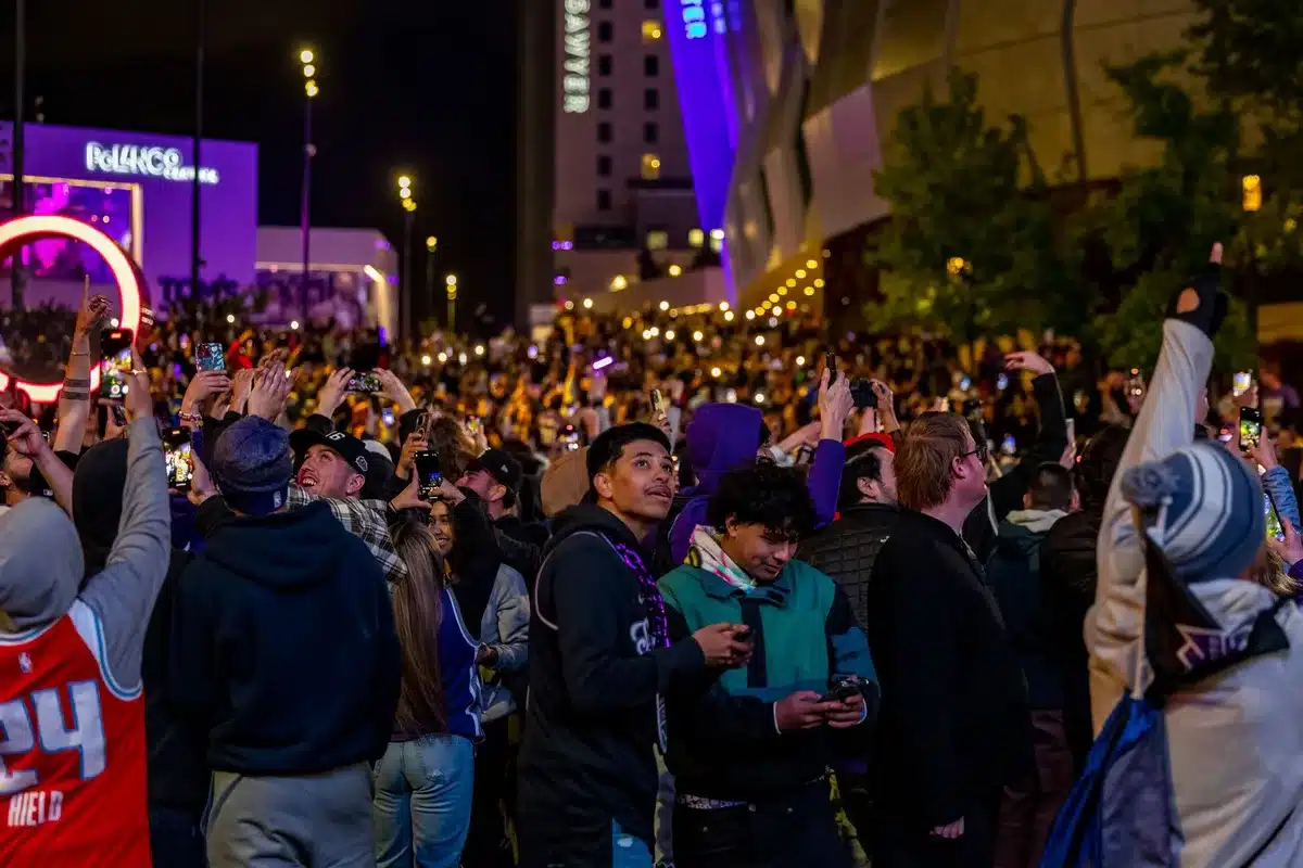 A crowded primary election watch party with supporters celebrating, raising fists and arms in jubilation at the moment of victory announcement, faces showing relief and excitement in warm indoor lighting