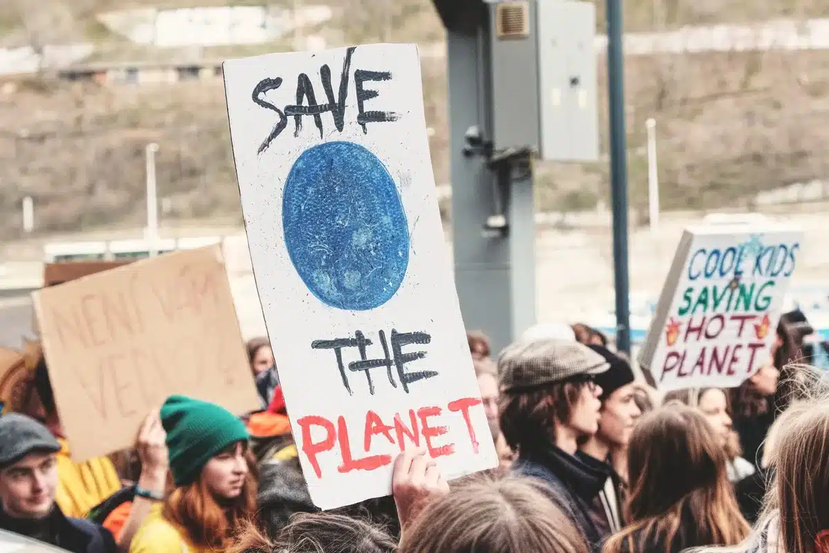 A progressive activist at a climate rally, holding a sign advocating for green energy policy, surrounded by supporters with raised fists, outdoor urban setting, sunlight catching dust in the air
