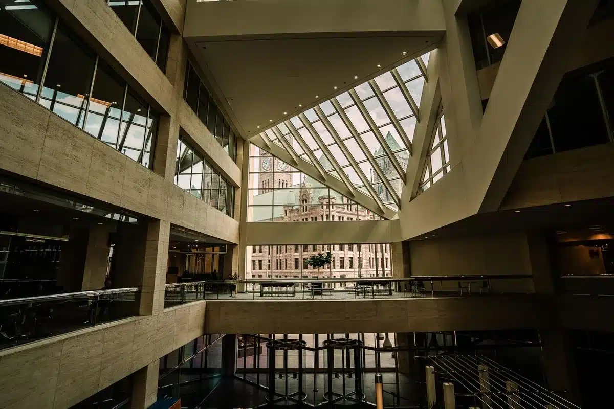 A modern office building representing a congressional office, glass windows reflecting a blue sky, empty corridor inside with flags on either side, suggesting political power and institutional authority