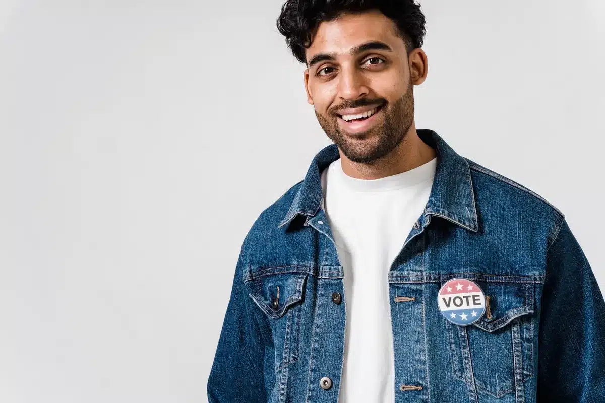 A diverse crowd of young voters gathered at a campaign rally, holding signs and banners, with raised arms showing enthusiasm and engagement