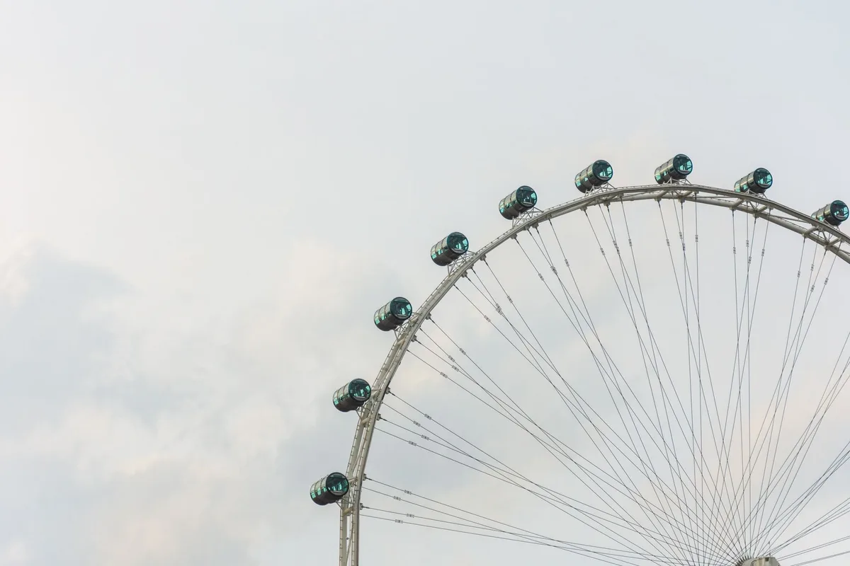 A towering observation wheel rising against a bright sky, with a sprawling fairground and distant cityscape visible from its peak, capturing the scale and vantage point of the ride.