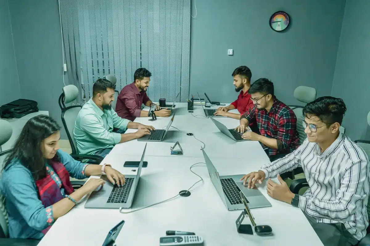An open notebook with hand-written notes about AI implementation, surrounded by physical documents and a laptop showing code or agent configuration screens in a modern office setting, representing enterprise AI planning and deployment