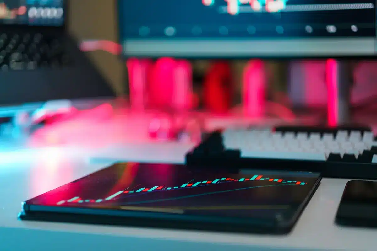 Modern office desk with multiple monitors displaying financial data and cryptocurrency charts, daylight through windows, professional fintech environment