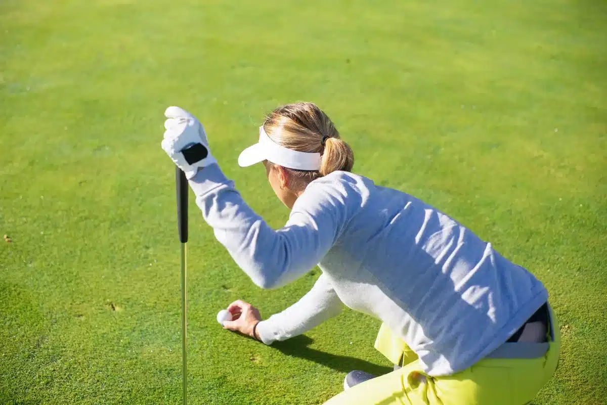 Golfer's hands gripping putter over the ball on the green, intense focus captured in soft natural light, concentration evident in body posture