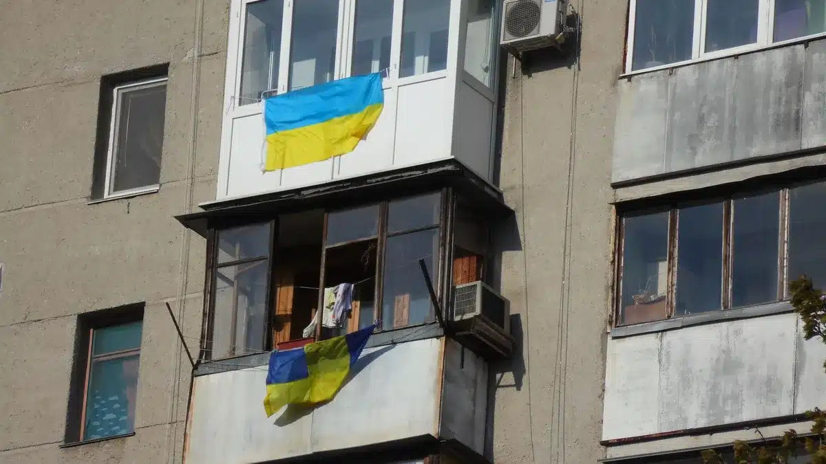 A Ukrainian flag hanging in a government building corridor, sunlight casting long shadows, suggesting the weight of ongoing diplomatic efforts and national resolve