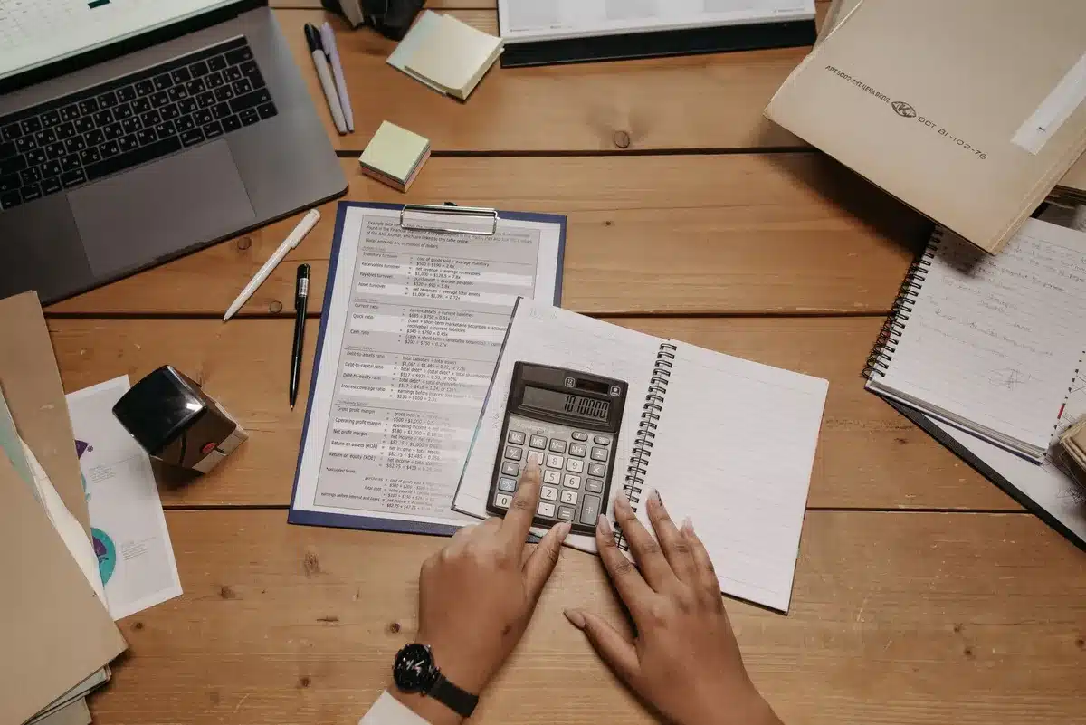 A computer screen displaying mortgage rate quotes and financial charts, with a calculator and loan documents scattered on a desk, neutral office lighting