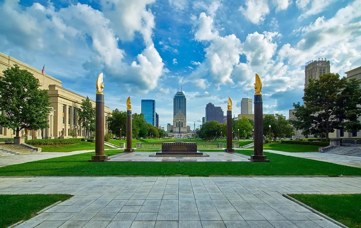A wide, empty memorial plaza at dawn with wreaths placed on a stone surface and a lone folded flag nearby, soft light and long shadows