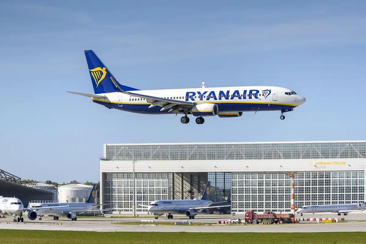 A wide empty gate area at a generic international terminal, a single unbranded jet parked at a distant jet bridge, maintenance carts nearby and staff silhouettes blurred in the far background