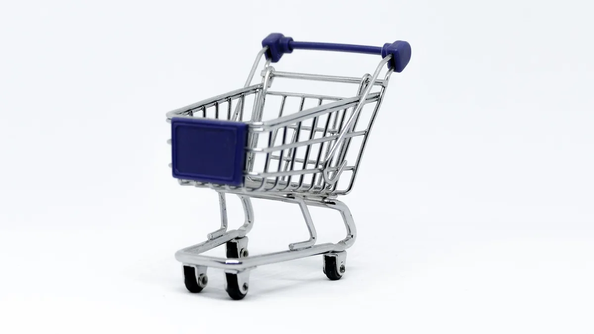Close-up of an unbranded shopping cart handle and a crate of generic oranges on a wooden display, empty register lanes in soft focus beyond
