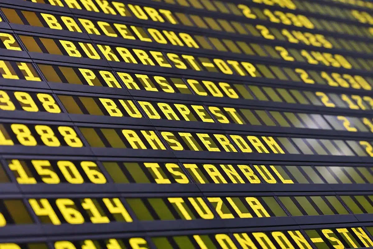An empty departure concourse with scattered luggage and distant, anonymous passengers waiting under overhead departure boards; no visible logos or airline branding