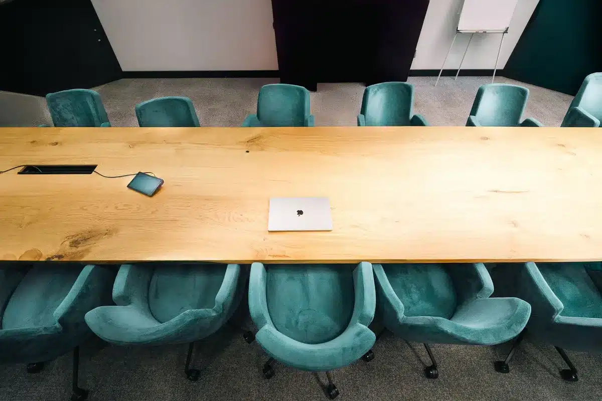 an empty modern boardroom table with a single unbranded laptop and a printed blank form labeled generically as a regulatory document, soft daylight through blinds