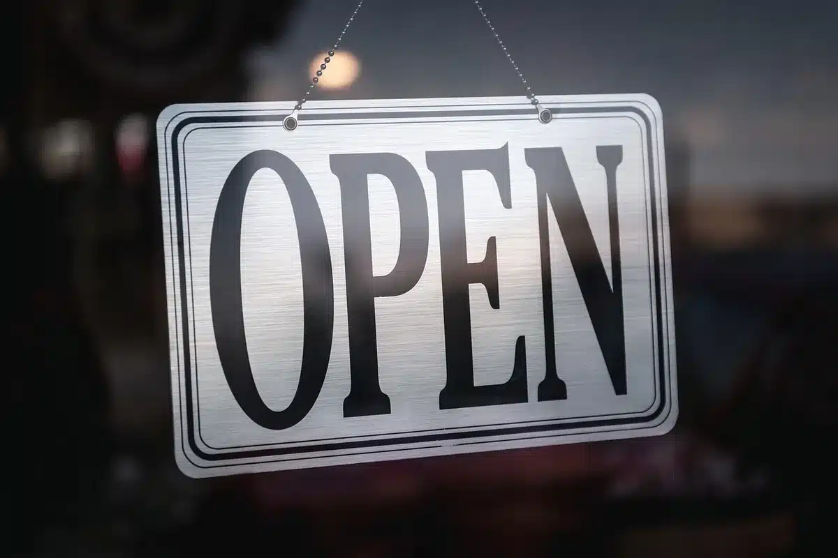 Modern glass storefront with clean lines and minimal signage, bright interior lighting reflecting off polished floors, display windows showcasing consumer electronics and products, anonymous shoppers browsing