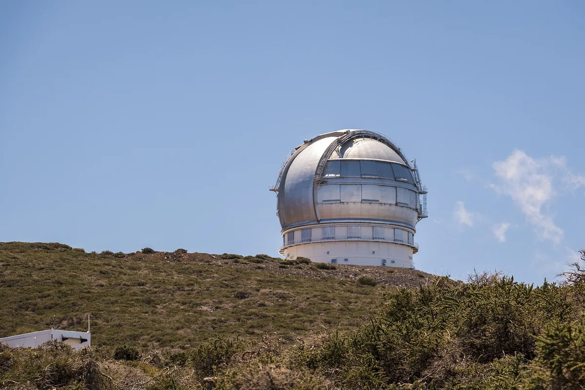 An anonymous wide-angle view of a night sky above a generic observatory dome, a telescope silhouette aimed upward with scattered stars and a faint streak suggesting a small asteroid — anticipation in a clear desert setting
