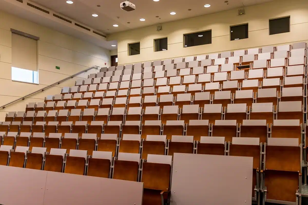 Empty rows in a large assembly hall with delegates' chairs visibly vacated, a single lectern in the distance under a spotlight