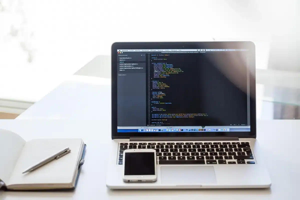A computer screen displaying cascading lines of code in green text on black background, a blurred figure's hand on a keyboard in the foreground, data streams flowing vertically, dim office lighting with a single desk lamp, abstract sense of AI systems operating beyond human control
