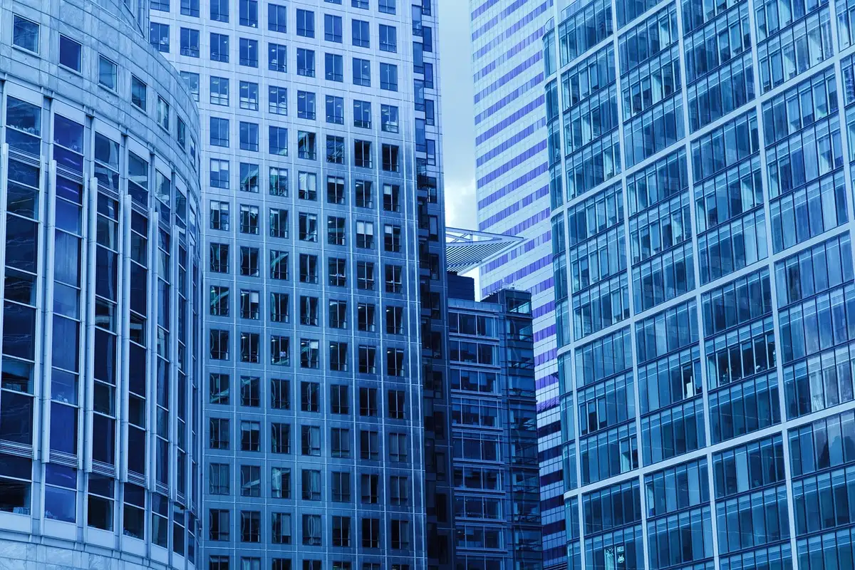 A modern glass and steel office building exterior at dusk with warm interior lighting visible through windows, suggesting a financial services headquarters