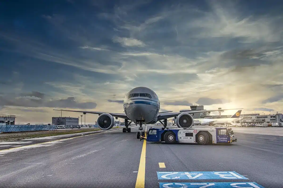 Anonymous silhouette of two airport technicians walking past an unbranded jet, rain-slick tarmac reflecting ramp lights, a distant cargo loader in motion