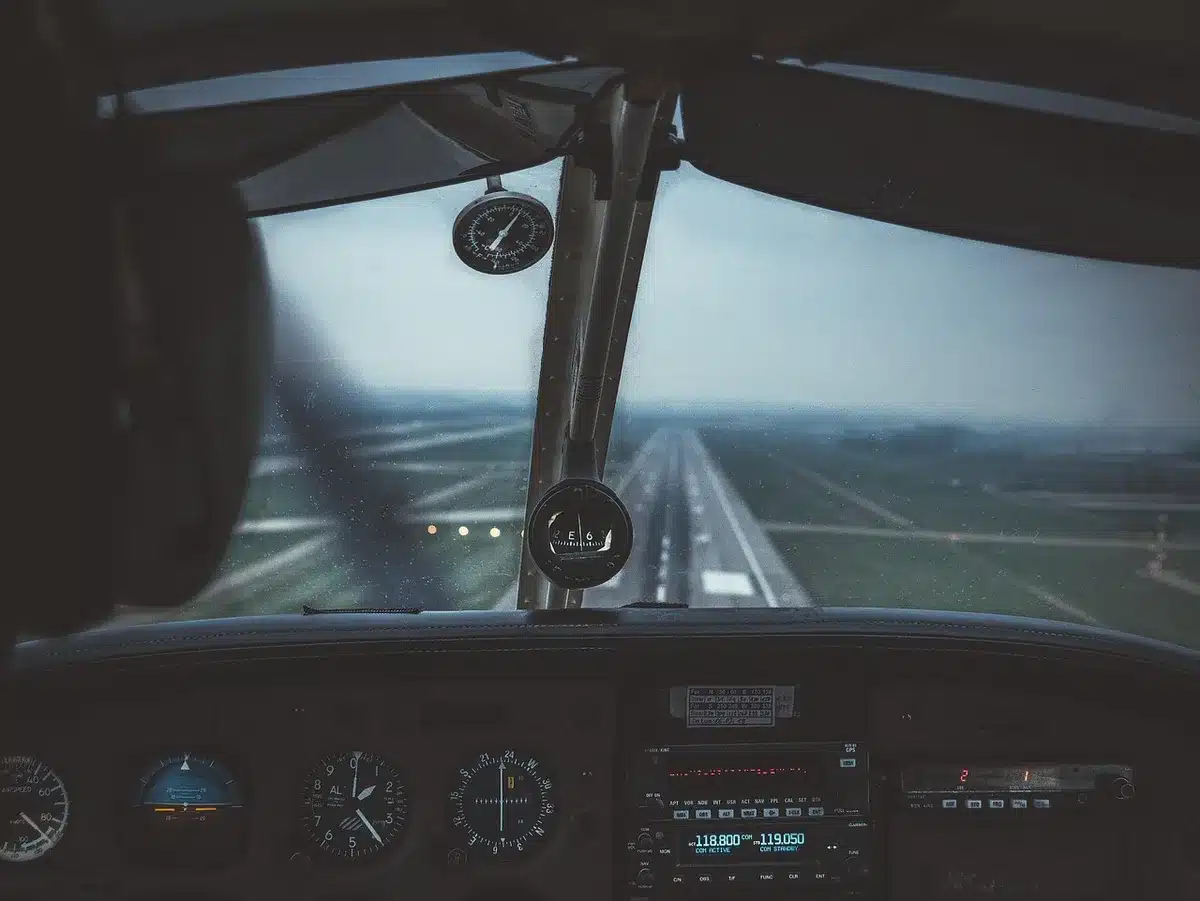 Interior of a commercial aircraft cockpit with visible avionics displays and instrument panels, showing complex navigation and control systems, natural light streaming through the windscreen