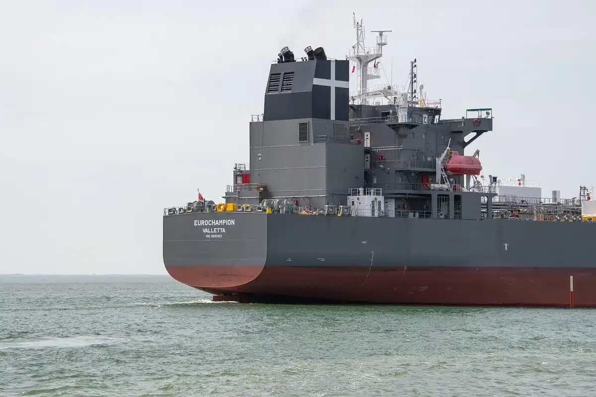 A cargo ship navigating narrow waters with warning lights, industrial tanker silhouetted against a stormy horizon, geographic chokepoint imagery