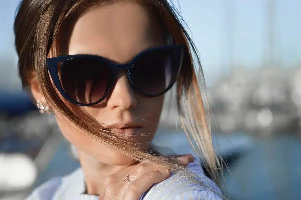 Close-up of glossy brunette hair strands catching warm light, showing dimensional layers of golden honey, caramel, and subtle copper tones blending seamlessly together. The shine and depth are the focal point.