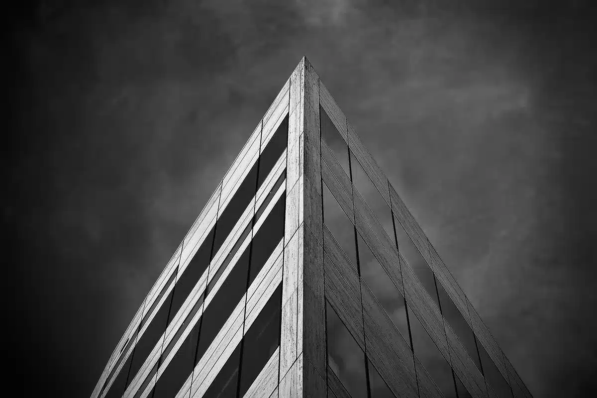 Gleaming glass tower rising into clear sky, geometric facade catching sunlight, urban landscape far below, sharp architectural lines disappearing into clouds