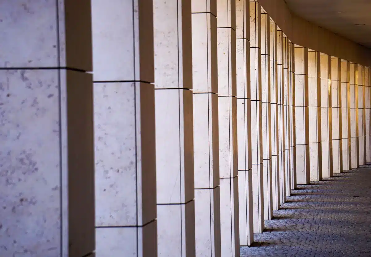 A lone, empty government office corridor with anonymous security doors, a folded map on a table and a single dim overhead light suggesting contingency planning