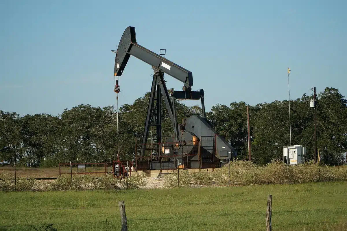 Oil extraction equipment and pipeline infrastructure in a tropical region, crude flowing through industrial piping under daylight, equipment maintenance crew visible in background