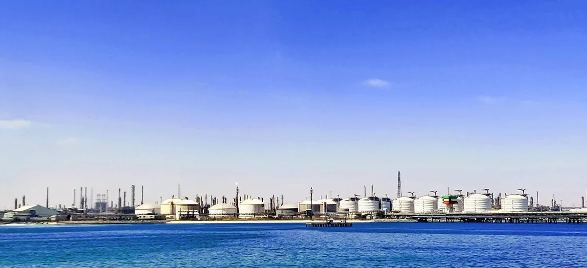 Refinery equipment and processing tanks at an industrial oil facility, steam rising from cooling towers, machinery silhouetted against industrial skyline